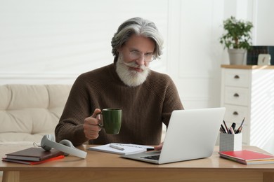 Middle aged man with laptop and cup of drink learning at table indoors