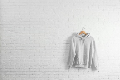 Photo of New hoodie sweater with hanger on brick wall. Mockup for design