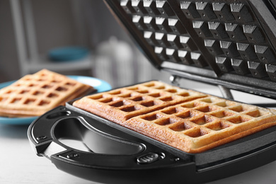 Photo of Modern iron with tasty Belgian waffles on table, closeup