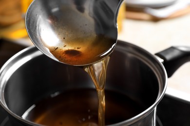 Photo of Pouring used cooking oil with ladle into saucepan on stove, closeup