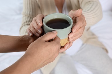 Caregiver giving drink to elderly woman at home, closeup