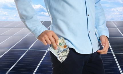 Man with money and installed solar panels on background, closeup. Economic benefits of renewable energy