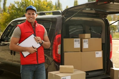 Courier with clipboard near car full of packages outdoors