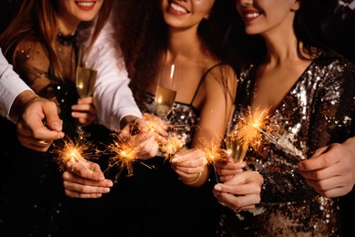 Photo of Friends with glasses of sparkling wine and sparklers celebrating New Year, closeup