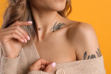 Beautiful woman with tattoos on body against yellow background, closeup