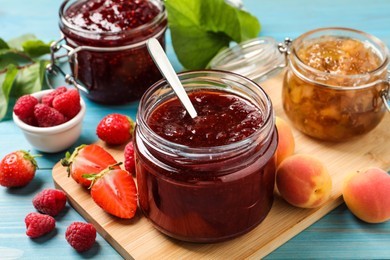 Jars with different jams and fresh fruits on light blue wooden table, closeup