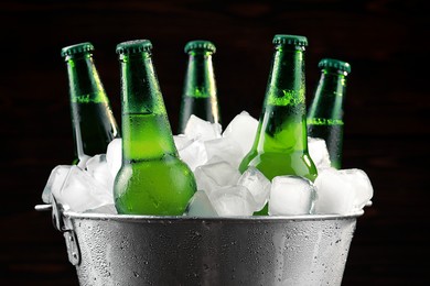Metal bucket with bottles of beer and ice cubes on dark background, closeup