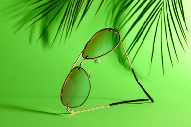 Stylish sunglasses and palm branches on green background