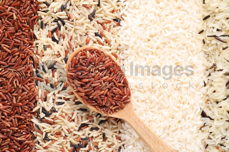 Different types of rice with wooden spoon, top view