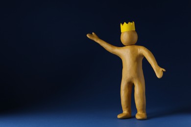 Plasticine figure with crown on head against dark blue background. Space for text