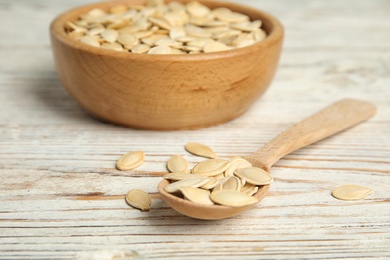 Raw unpeeled pumpkin seeds on white wooden table, closeup