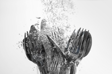 Photo of Washing silver cutlery in water on white background