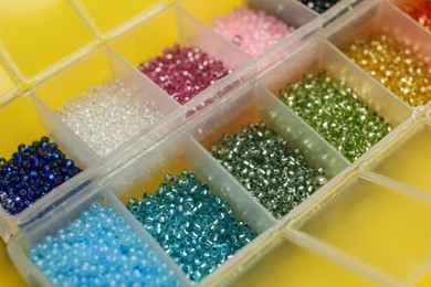 Organizers with variety of colorful beads on yellow background, closeup