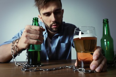 Addicted man chained to glass of alcoholic drink at wooden table, focus on hands