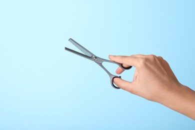 Hairdresser holding professional thinning scissors on turquoise background, closeup. Haircut tool