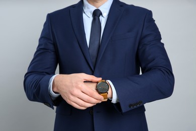 Businessman wearing wristwatch against grey background, closeup. Time management