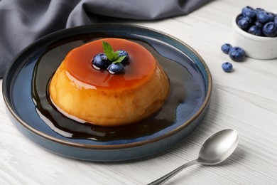 Photo of Plate of delicious caramel pudding with blueberries and mint served on white wooden table
