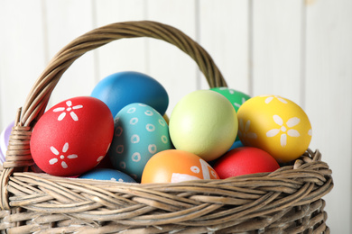 Colorful Easter eggs in wicker basket against light background, closeup