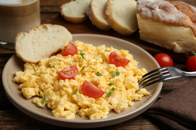Tasty scrambled eggs with cherry tomato and bread on wooden table, closeup