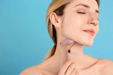 Photo of Young woman using natural rose quartz face roller on light blue background, space for text