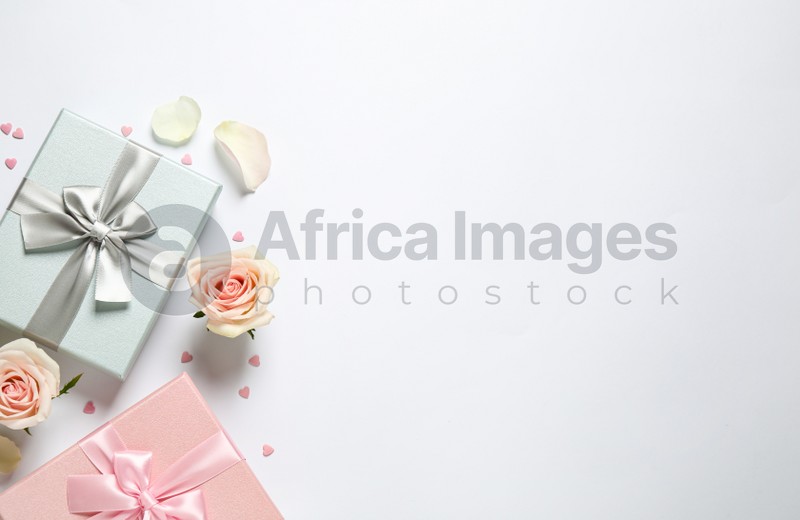 Elegant gift boxes and beautiful flowers on white background, flat lay. Space for text