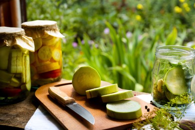 Photo of Cut fresh zucchini and jars of pickled vegetables on wooden table