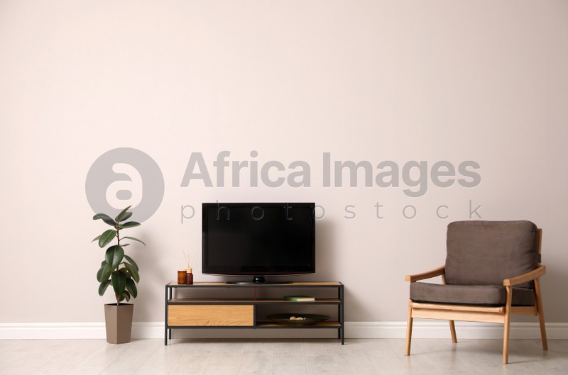 Photo of Elegant room interior with TV on cabinet, houseplant and armchair near light wall