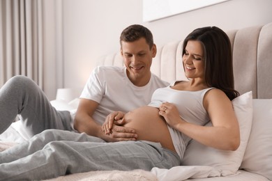 Photo of Young pregnant woman with her husband in bedroom