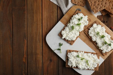 Photo of Crispy crackers with cottage cheese and microgreens on wooden table, flat lay. Space for text