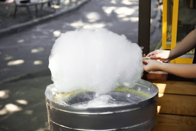 Photo of Woman making cotton candy using modern machine outdoors, closeup