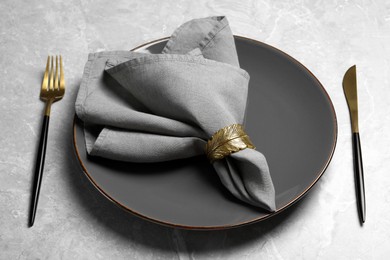 Plate with fabric napkin, decorative ring and cutlery on light gray marble table