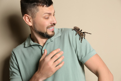Photo of Scared man with tarantula on beige background. Arachnophobia (fear of spiders)