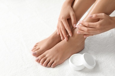 Woman with beautiful feet and moisturizing cream on white towel, closeup. Spa treatment