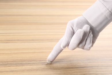 Person in white glove checking cleanliness of wooden  table, closeup