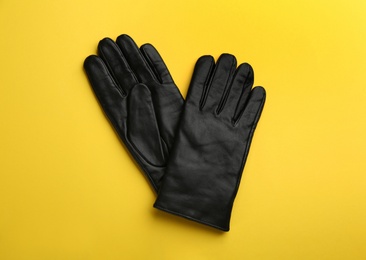 Pair of stylish leather gloves on yellow background, flat lay