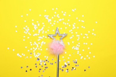 Beautiful silver magic wand with feather and confetti on yellow background, flat lay