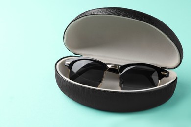 Stylish sunglasses in black leather case on light blue background