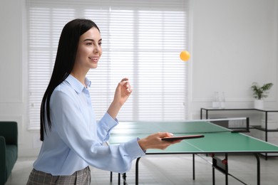 Business woman with tennis racket and ball near ping pong table in office