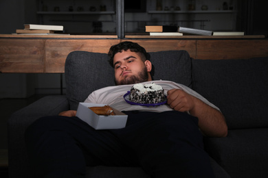 Depressed overweight man with sweets in living room at night