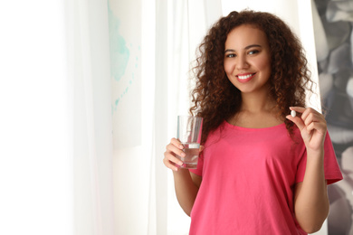 Photo of African-American woman with glass of water and vitamin pill indoors. Space for text