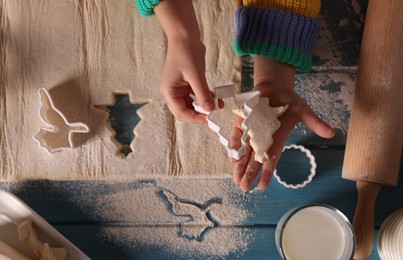 Little child making Christmas cookies at blue wooden table, top view