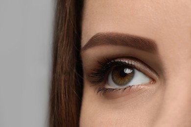 Young woman with beautiful eyes on grey background, closeup view