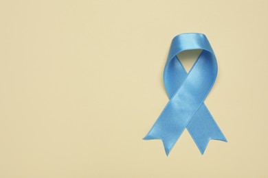 Photo of Light blue awareness ribbon on beige background, top view. Space for text