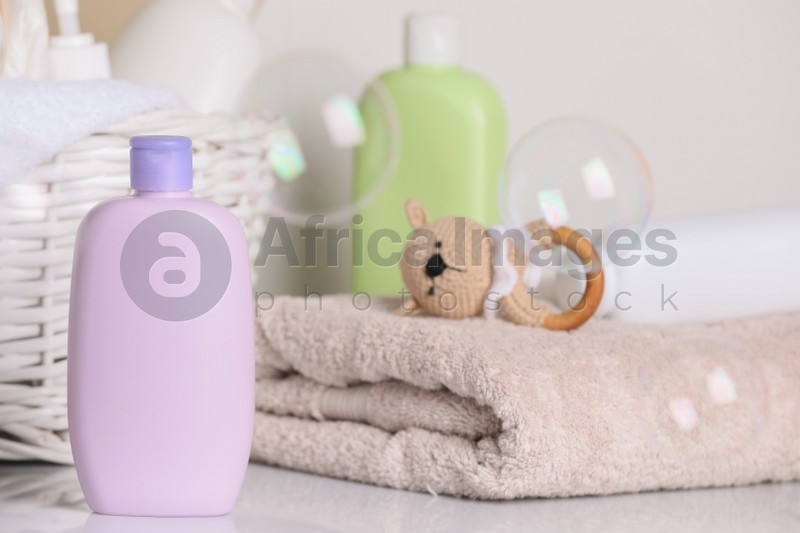Photo of Baby cosmetic products, towel, toy and soap bubbles on light background