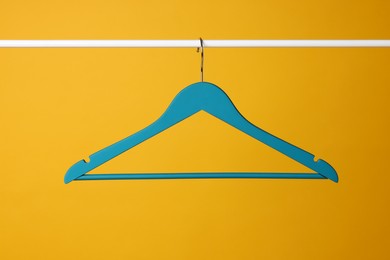 Empty clothes hanger on metal rail against yellow background