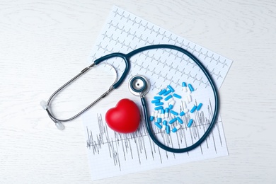 Stethoscope, heart, pills and cardiograms on wooden background, top view. Cardiology concept