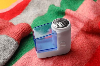 Photo of Modern fabric shaver on colorful knitted sweater, closeup