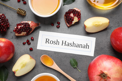 Card with text ROSH HASHANAH, apples, honey and pomegranates on grey table, flat lay
