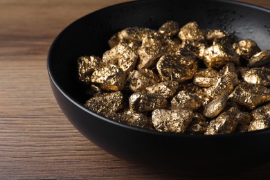 Bowl of gold nuggets on wooden table, closeup