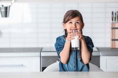 Cute little girl drinking milk at table in kitchen